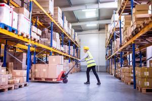 Young woman warehouse worker with hand forklift truck.