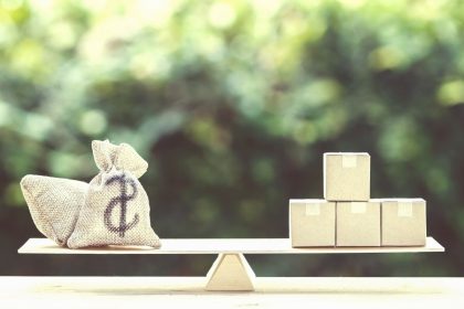 Money dollar bag and supply products on balance scale on wooden