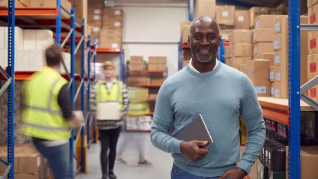 Portrait Of Manager With Digital Tablet In Busy Modern Warehouse With Staff In Background VMI to mitigate geopolitical risk in supply chain