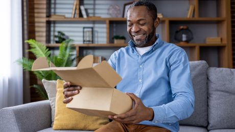 Smiling man unboxing a package while sitting on a couch at home how a 3PL improves performance