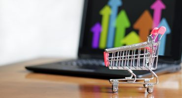 Closeup of a small shopping cart on the table with a laptop on it – concept of online shopping
