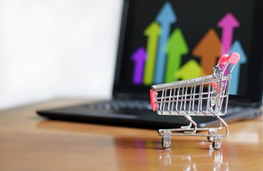 Closeup of a small shopping cart on the table with a laptop on it – concept of online shopping