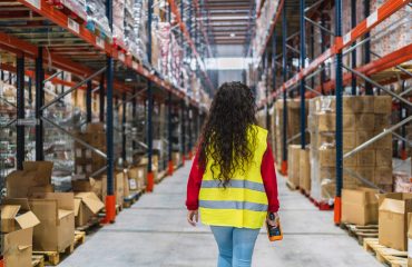 Female warehouse worker walking through storage area holding scanner shared vs. dedicated warehousing