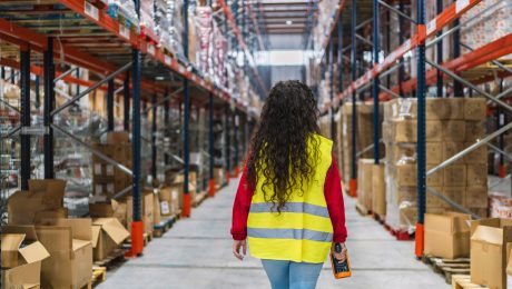 Female warehouse worker walking through storage area holding scanner shared vs. dedicated warehousing
