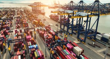 Container ship docked at port with cargo trucks and cranes. Global logistics hub. Maritime freight operations. International trade and supply chain management. Import-export terminal. Global commerce. inverted tariff trap